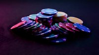 Colorful casino poker chips stacked on dark felt table surface for gambling entertainment and gaming industry promotional materials.