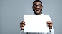Excited African American man with glasses holding blank white sign against gray background, perfect for adding custom message or promotional content.