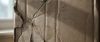 Damaged brown cardboard box with torn edges and cracks showing wear from shipping or storage in warehouse environment.