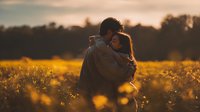 Young man photographer capturing golden hour sunset in wildflower meadow with professional camera equipment during magic hour lighting conditions.
