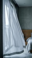 Sheer gray linen curtains hang elegantly in a modern bedroom with concrete walls and wooden bed frame, filtering soft natural light for contemporary home decor and interior design.