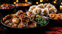 Glazed Asian chicken with sesame seeds and steamed vegetables served on dark plate with dumplings and festive holiday decorations in background.