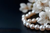 Elegant pearl necklace with delicate white cherry blossoms against dark background, creating luxurious jewelry composition with soft natural lighting.