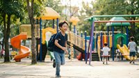 Young Asian boy running joyfully at colorful playground with slides and climbing equipment in sunny park setting for active childhood recreation.