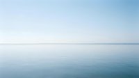 Serene calm water surface with clear sky horizon, minimalist seascape for peaceful backgrounds and meditation content.
