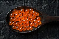 Fresh red caviar spheres arranged in wooden spoon on dark stone background, luxury seafood delicacy for gourmet appetizer and fine dining.