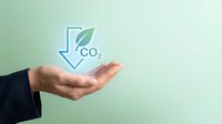 Businessman hand presenting carbon dioxide reduction concept with leaf and downward arrow symbol for environmental sustainability and climate action.