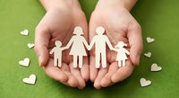 Hands protecting wooden family figures on green background with hearts. Care, support and love concept for insurance, adoption and family values.