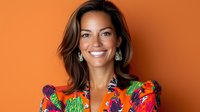 Smiling woman wearing vibrant floral print blouse against orange background. Professional headshot with natural makeup and wavy brown hair showcases confident, friendly expression.