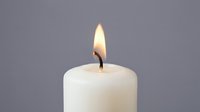 White candle with bright flame burning against neutral gray background for relaxation, meditation, spa treatments, aromatherapy and peaceful ambiance.