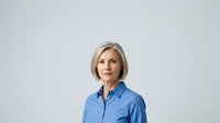 Middle-aged woman with shoulder-length blonde hair and fair complexion wearing a light blue button-up shirt against a neutral gray background. Professional headshot suitable for corporate, business, and portrait use.