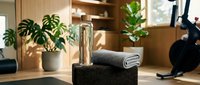 Spa wellness setup with rolled towel, water bottle and potted plants on black stone pedestal in modern wooden interior for relaxation and self-care concepts.