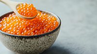 Fresh red caviar in ceramic bowl and spoon on gray background, luxury seafood delicacy with bright orange salmon roe pearls, gourmet appetizer close-up.