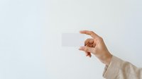 Hand holding blank white business card against neutral background, suitable for branding, corporate identity, and marketing mockup designs.