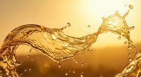 Golden liquid splash with dynamic flowing motion and droplets against warm amber background for beverage and fluid dynamics concepts.