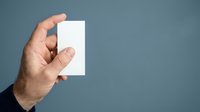 Male hand holding blank white card against gray background. Isolated mockup for business card, ticket, or promotional material design.