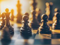Wooden chess pieces on board in warm golden light with selective focus on pawns and queen, creating atmospheric mood for strategy and leadership concepts.