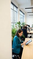 Professional businesswoman using tablet in modern office workspace with plants and natural light for corporate presentations and meetings.