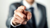 Businessman in formal suit pointing finger directly at viewer, conveying leadership, recruitment, or accountability in professional corporate setting.