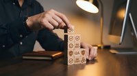 Businessman stacking wooden blocks with quality control icons representing business standards and process improvement in modern office environment.