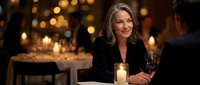 Elegant mature woman enjoying wine at upscale restaurant with warm candlelight ambiance for romantic dining and hospitality marketing materials.