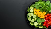 Fresh colorful salad bowl with sliced cucumber, red bell pepper, mango cubes and spinach leaves on dark background, healthy eating concept.