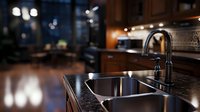 Modern kitchen interior with double basin stainless steel sink and black faucet on dark granite countertop, evening mood lighting creates cozy atmosphere.