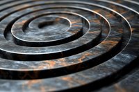 Dark metallic spiral coils with rust patina creating concentric circles pattern for industrial design backgrounds and textures.