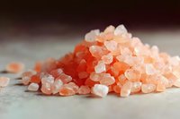 Pink Himalayan salt crystals scattered on light surface with soft focus and shallow depth of field, natural mineral seasoning in warm lighting.