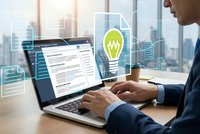 Professional businessman working on laptop with green lightbulb innovation icon overlay in modern office environment for creative business solutions.