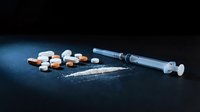 Drug addiction concept with syringe, pills and white powder on dark surface for awareness campaigns and educational materials.