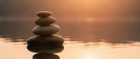 Balanced stack of smooth river stones creating zen meditation tower against serene water surface during golden hour sunset for wellness and mindfulness concepts.