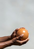 Hand holding fresh brown egg against neutral background, isolated on white. Suitable for food, nutrition, cooking, and healthy eating concepts.