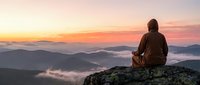 Person meditating on mountain peak at sunrise with misty valleys below, peaceful morning landscape for wellness and mindfulness concepts.