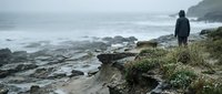 Solitary figure standing on dramatic coastal cliff overlooking stormy ocean waves with moody overcast sky for contemplative outdoor adventure themes.