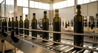 Olive oil bottles moving on industrial conveyor belt in modern food processing factory with natural lighting and stainless steel equipment for production.