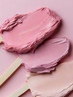 Pink cosmetic cream swatches with wooden applicators on matching background, showcasing makeup texture and color variations for beauty product presentation.