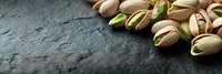 Fresh roasted pistachio nuts scattered on dark stone background with copy space, macro food photography for healthy snack advertising.
