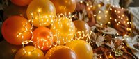 Glowing happy birthday sign with warm golden and orange balloons decorated with fairy lights, creating a festive autumn celebration atmosphere.