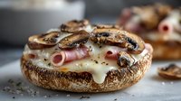 Stuffed portobello mushroom cap topped with melted cheese, sliced mushrooms and ham rolls on kitchen counter ready for gourmet meal preparation.