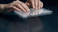 Close-up of hands typing on transparent holographic keyboard interface against dark background, representing futuristic technology and digital innovation.