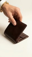 Male hand with gold watch reaching for brown leather wallet on white background for business and finance concepts.