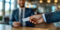 Business professional receiving business card from colleague in modern office setting with blurred background and natural lighting.