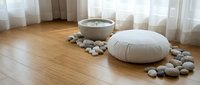 Zen meditation space with white cushion, singing bowl and smooth stones on wooden floor creating peaceful mindfulness atmosphere for relaxation and wellness.