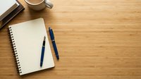 Minimalist workspace with open notebook, blue pen and coffee cup on wooden desk surface with copy space for productivity and planning concepts.