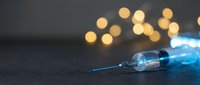 Medical syringe with blue liquid glowing on dark surface with warm bokeh lights in background for healthcare and pharmaceutical concepts.