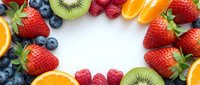 Colorful fresh fruit frame with strawberries, blueberries, kiwi, orange slices and raspberries arranged in circle on white background for healthy eating.