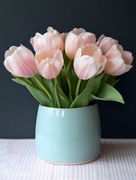 Fresh pink tulips arranged in mint green ceramic vase on white surface against dark background for spring home decor and floral arrangements.