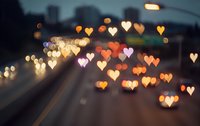 Heart-shaped bokeh lights create romantic atmosphere over blurred city street at dusk with warm golden and orange glowing effects for Valentine's Day designs.