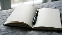 Open blank notebook with black pen on bed ready for writing thoughts ideas journaling creative work planning goals daily tasks personal reflection.